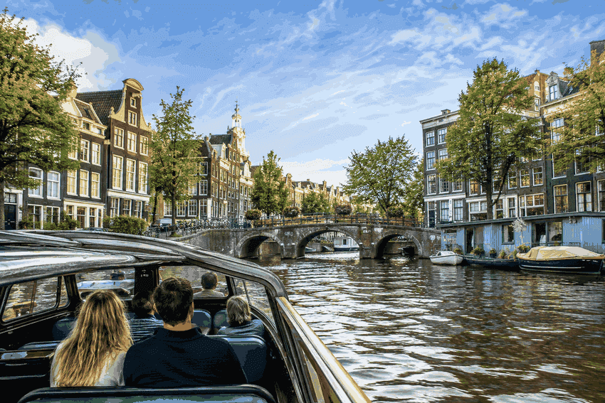Amsterdam canal cruise with passengers passing historic canal houses and arched bridges in the city centre.
